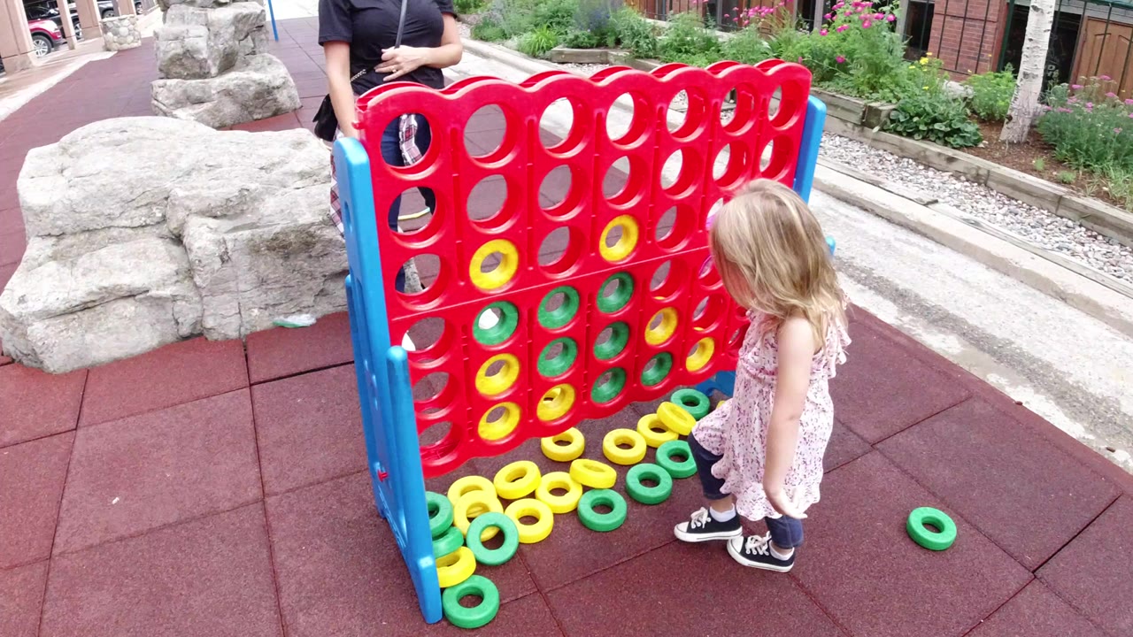 Young girl beside a giant red playground game with yellow and green rings.