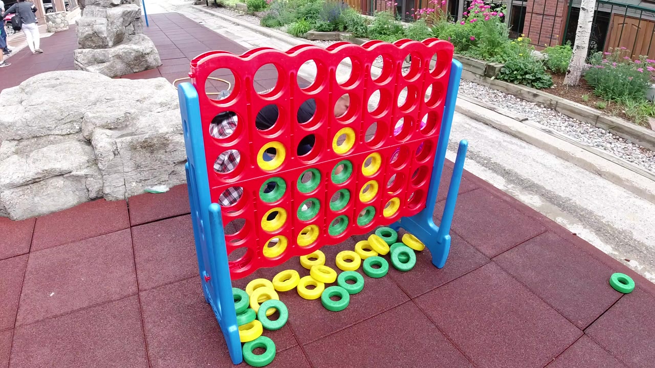 Oversized red Connect Four game with green and yellow rings on red paving.