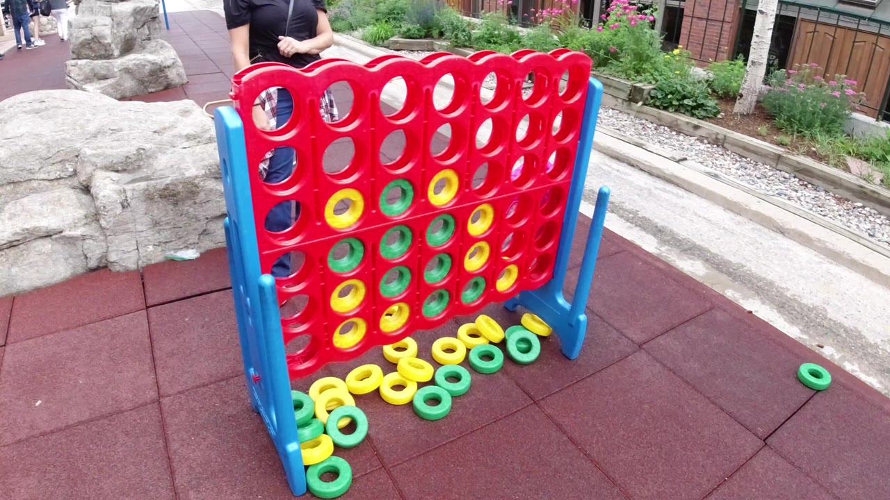 The large red game board remains centered in Winter Park, Colorado, with yellow and green rings loaded into several lower holes and extra rings lying along the base.