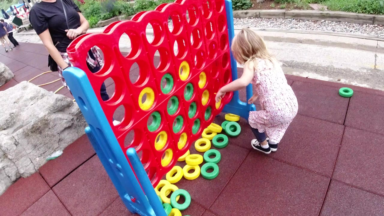 In Winter Park, Colorado, the child bends near a blue side support of the red game board, with several yellow and green rings scattered below the slots and a walkway behind.