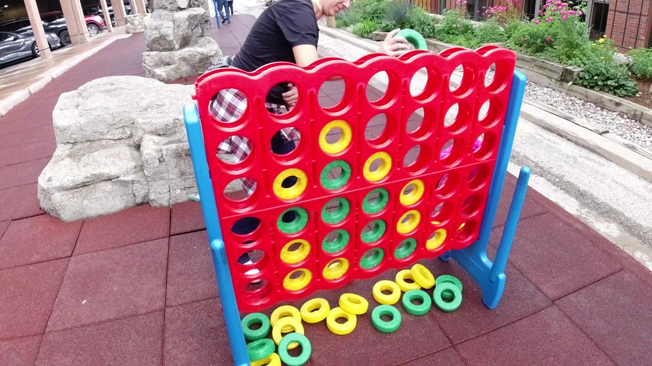 Adult and child beside a large red outdoor game board with yellow and green rings.