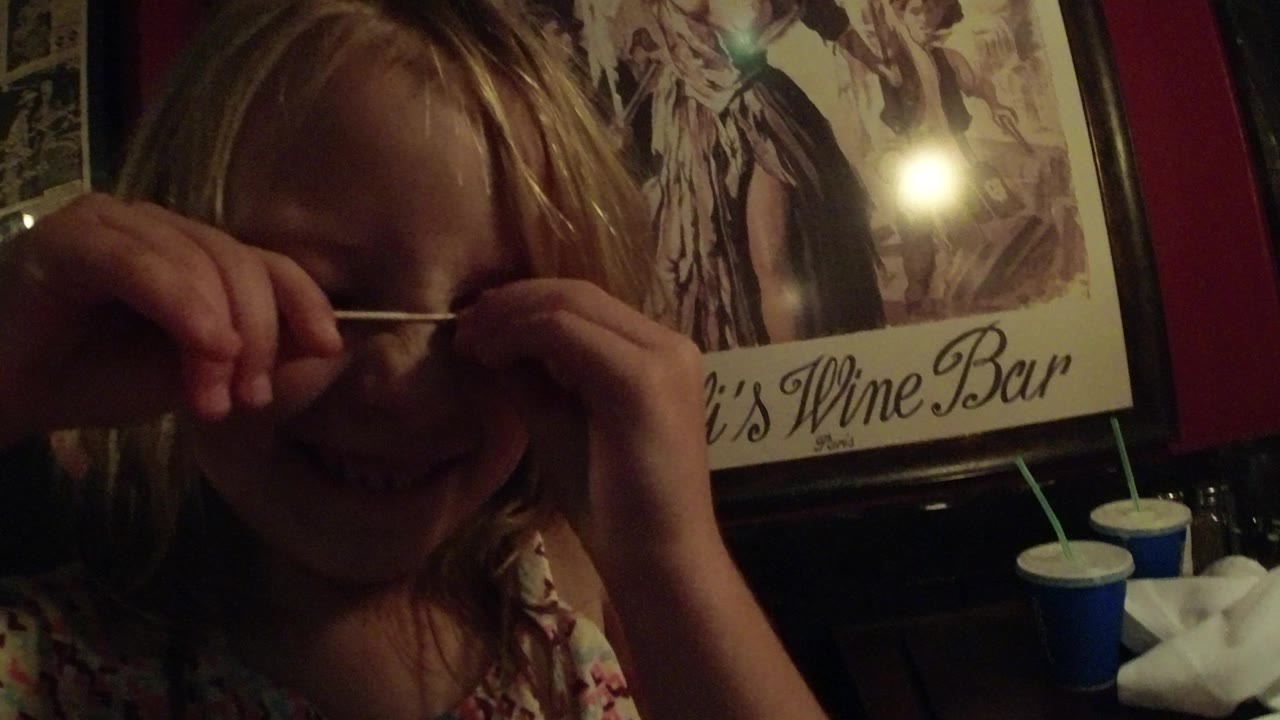 Young blonde girl holding a stick across her face indoors.