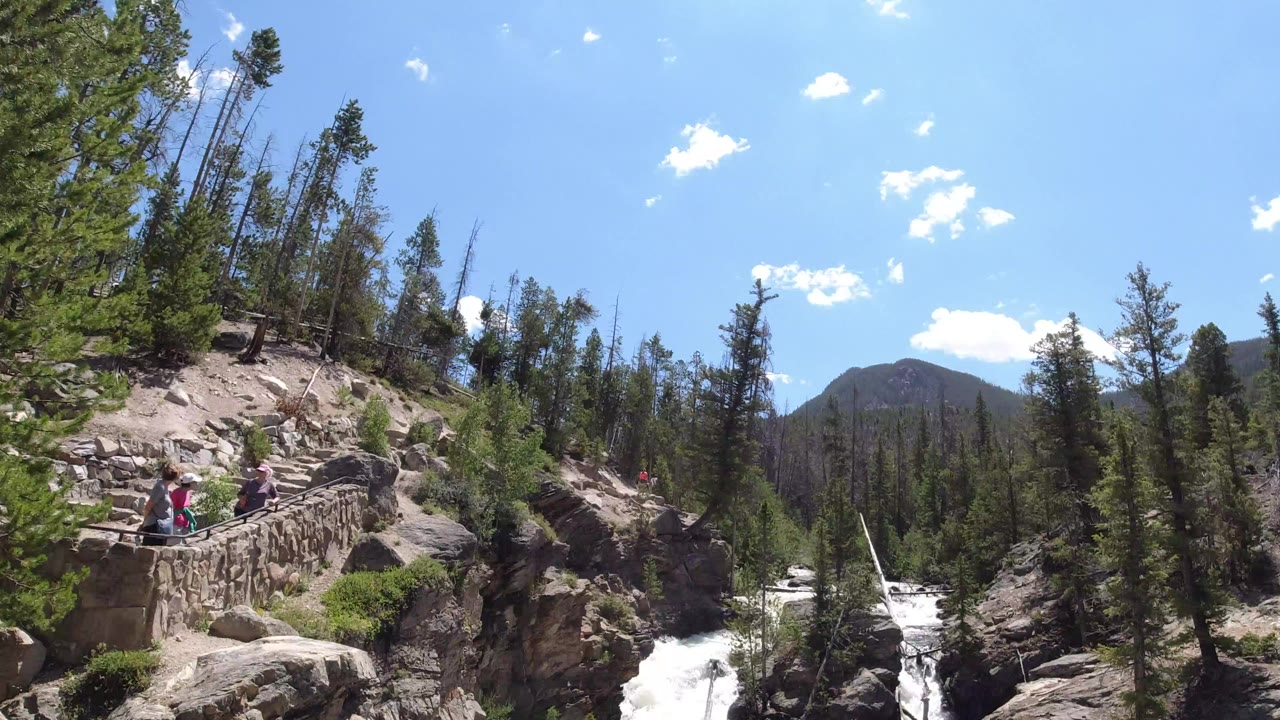 Wide view of rapids below a rocky overlook and pine trees.