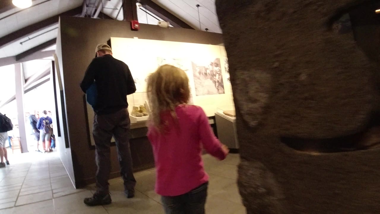 In Winter Park, Colorado, the child moves farther into the gallery, with the large rock-textured display blocking part of the middle frame and an adult standing near a lit exhibit case.