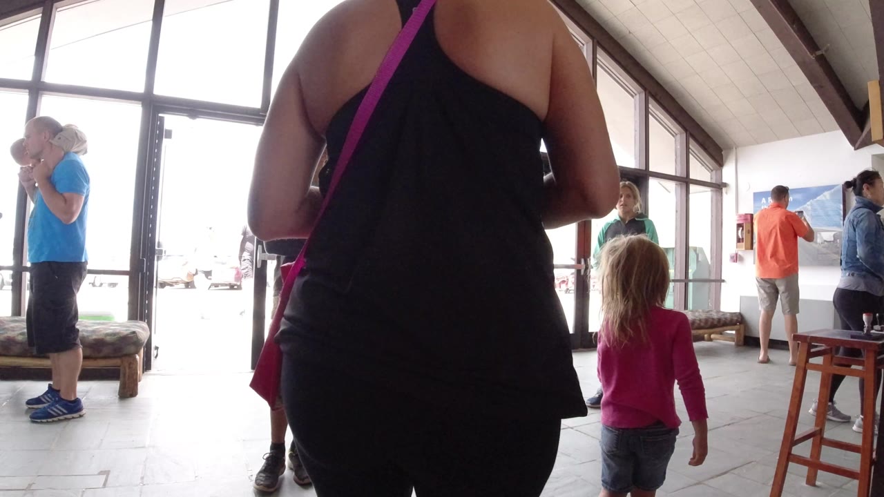 Inside a Winter Park, Colorado interior, a young girl in pink stands near an older woman in black while several adults gather by tall glass doors.