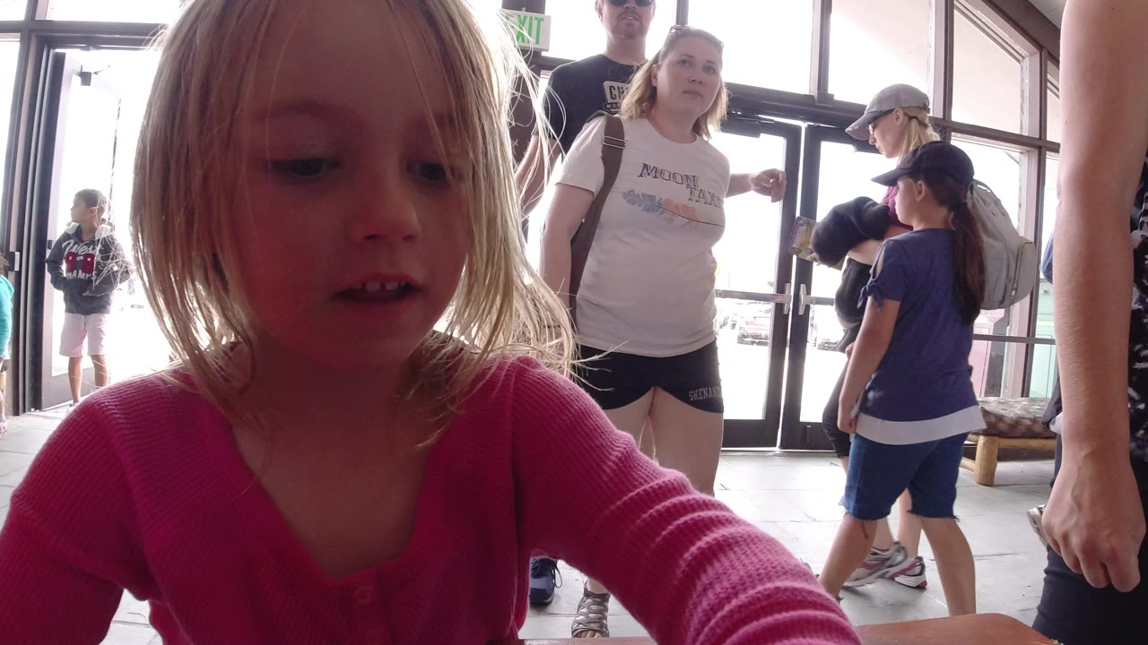 The child remains in the foreground at table level in Winter Park, Colorado, as a small crowd stands in the backlit doorway area behind her.