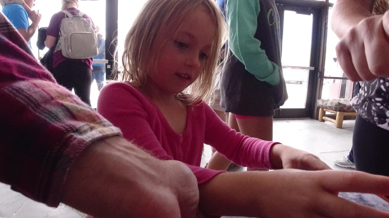 In Winter Park, Colorado, the girl stays focused on the tabletop while an adult hand in a plaid sleeve presses close to her outstretched hand.