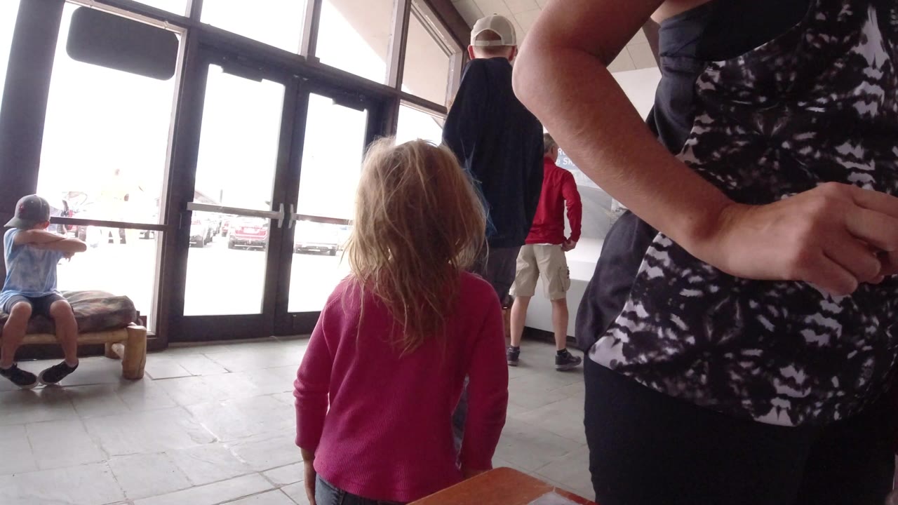 Visitors stand and sit near large glass doors inside a Winter Park, Colorado museum or visitor-center interior, with a child in a pink top in the foreground.