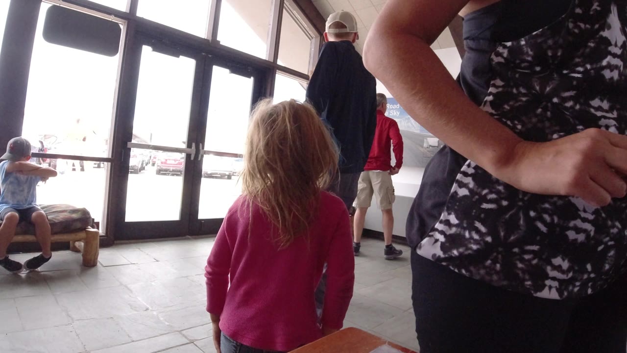 A child in a pink top stands near adults in the bright Winter Park, Colorado interior, with glass doors and benches still visible behind them.
