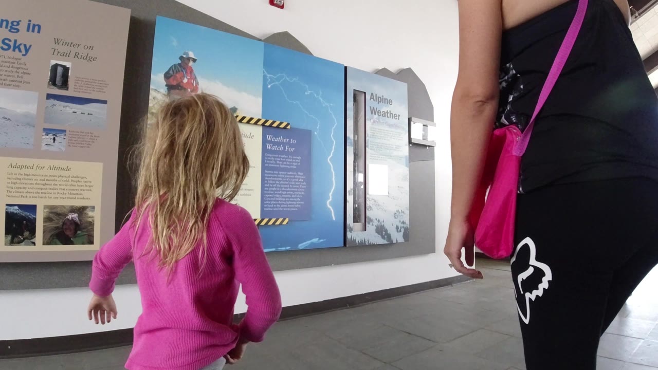 In Winter Park, Colorado, the girl moves farther along the exhibit wall as high altitude safety and weather panels fill the background.