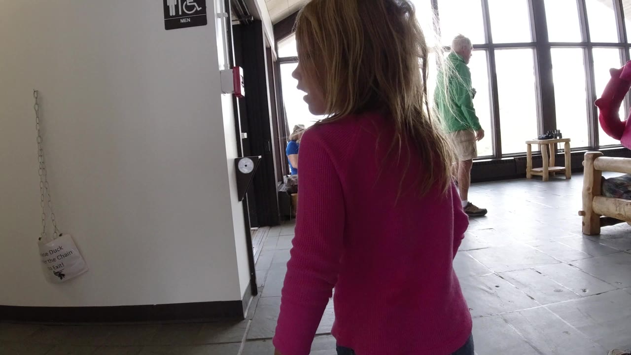 Young girl in a pink top near an indoor doorway and tall windows.