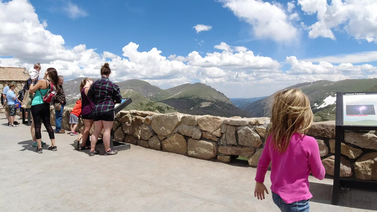 Visitors at a stone-walled mountain overlook under bright clouds.