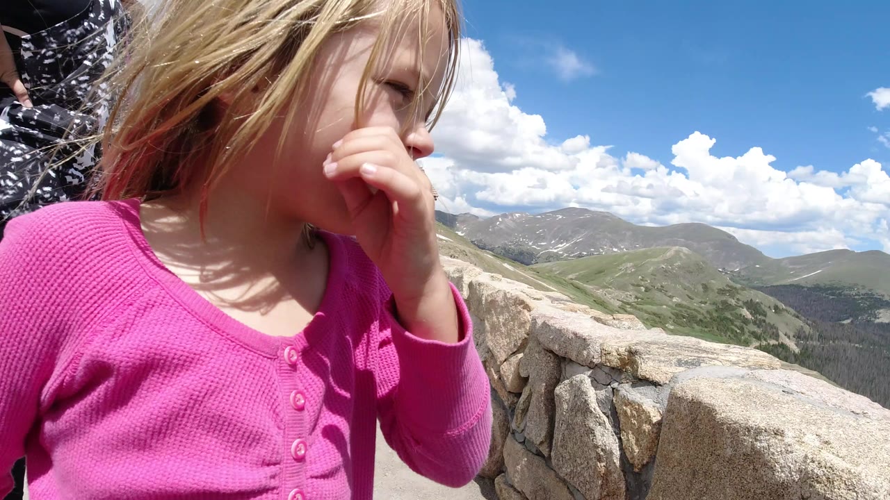 Child in pink near a stone overlook wall with mountains behind.