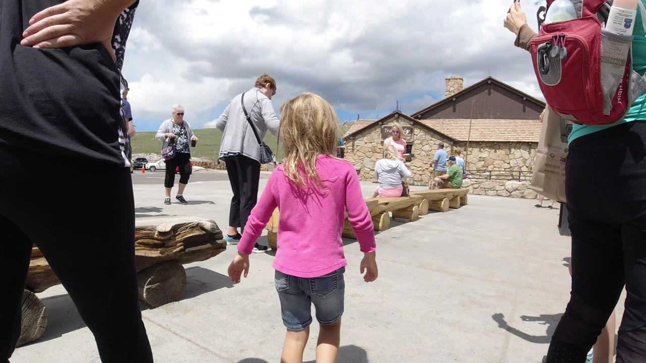 Child in a pink shirt walking between adults at a mountain overlook.