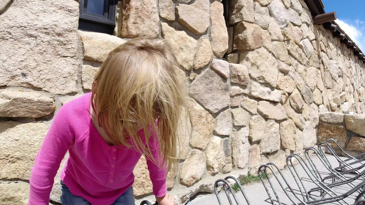 The child remains close in the foreground beside the arranged metal chairs, with the stone building wall filling most of the background in Winter Park, Colorado.