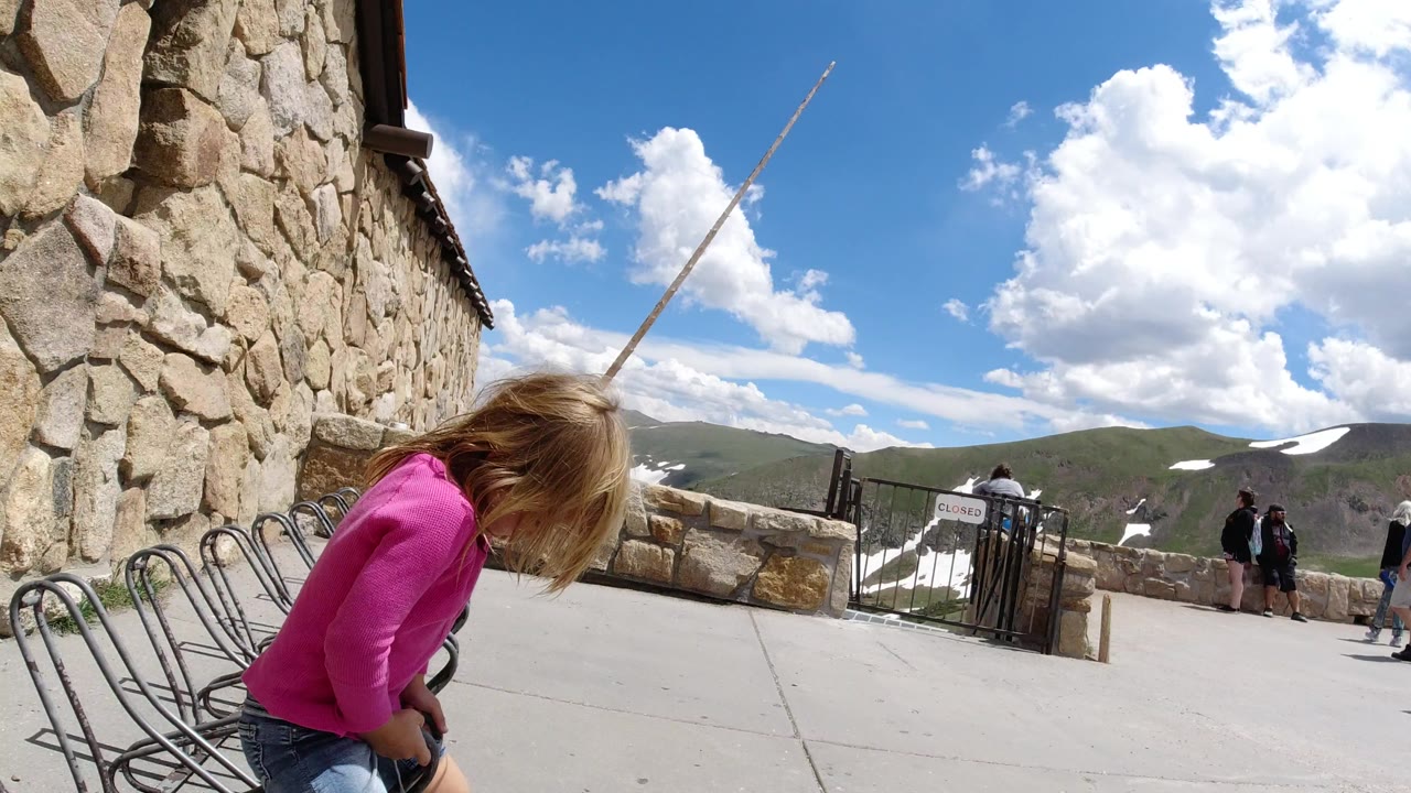 Child in a pink top bends near bike racks beside a stone wall at a mountain overlook.