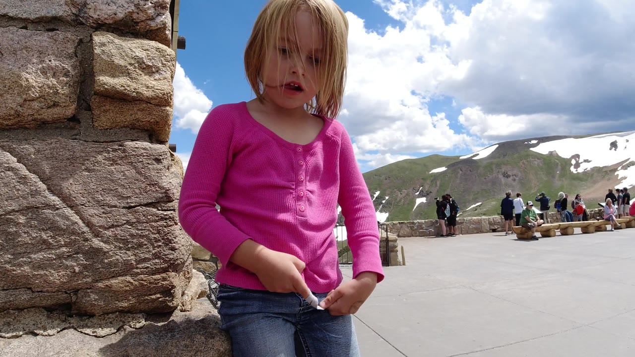 The child faces more toward camera while holding the string at the Winter Park, Colorado overlook, with her hair partly across her face and distant visitors along the railing.