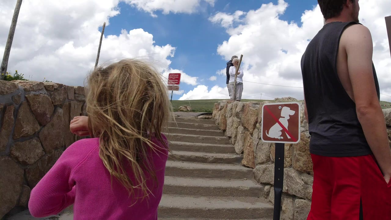Girl in a pink top faces outdoor steps beside a man in red shorts.