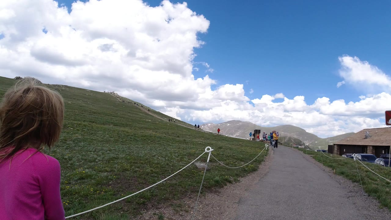 Girl in pink walking beside a roped hillside path under clouds.