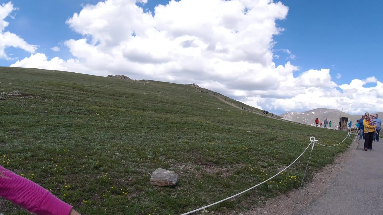 Rope-lined mountain path with visitors in the distance and part of a pink sleeve at the edge.