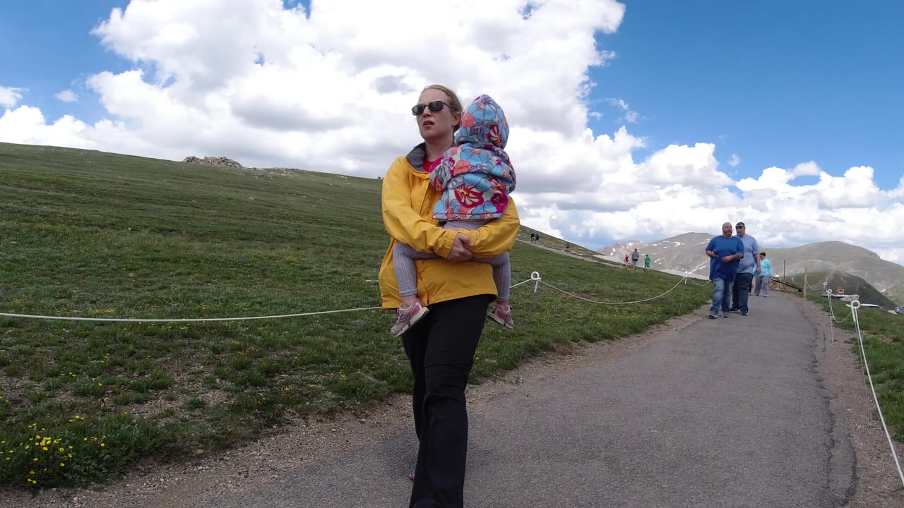 A woman carrying a child remains near the center of the Winter Park, Colorado frame while two adults approach on the path beneath a cloud-filled sky.