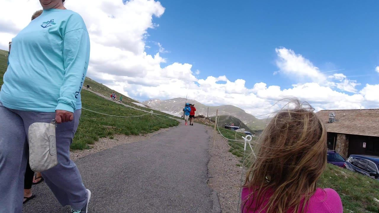 Adult and child near a paved mountain path under a cloudy blue sky.
