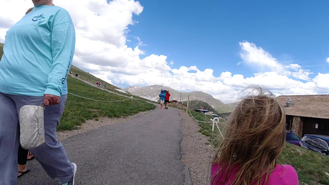 A child in a pink top stands near the camera on the Winter Park path while a cropped adult remains at left and two walkers appear farther uphill.