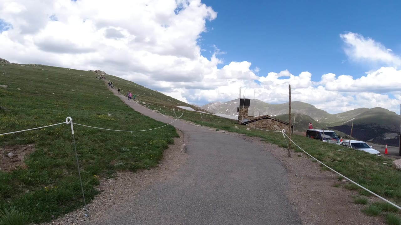 Uphill paved sidewalk through grassy mountain slope with distant pedestrians.