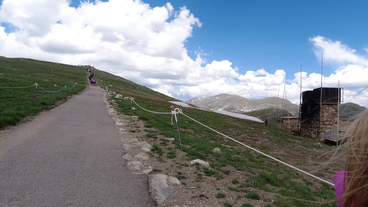 Uphill paved path through green mountain slopes under clouds.
