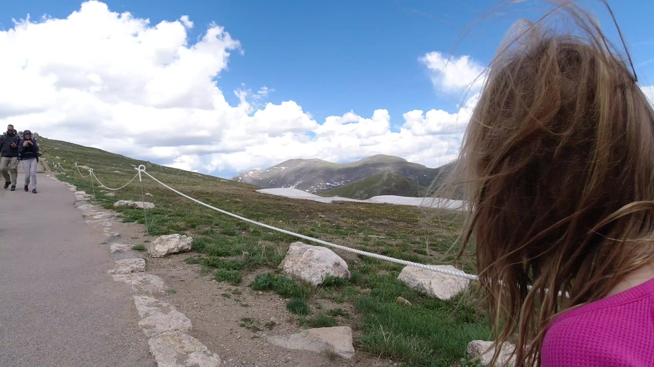 Girl in pink seen from behind on a mountain path.