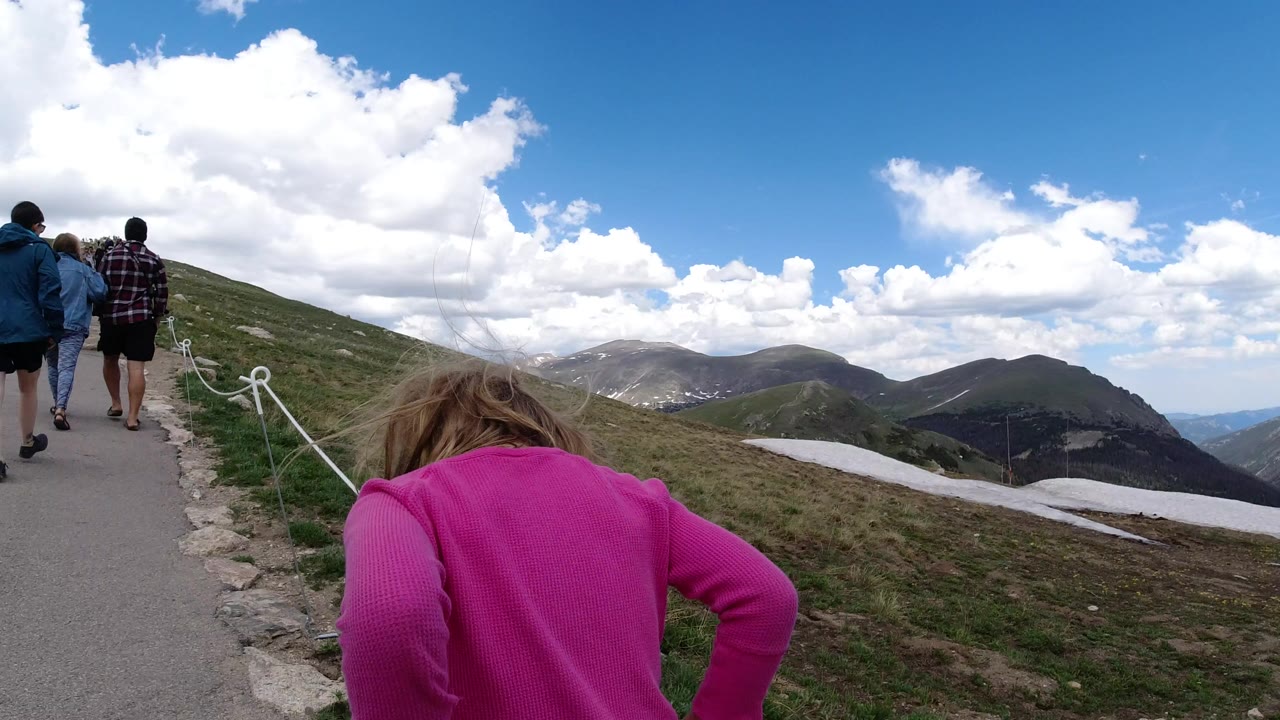 Child in pink walking behind people on a mountain path.