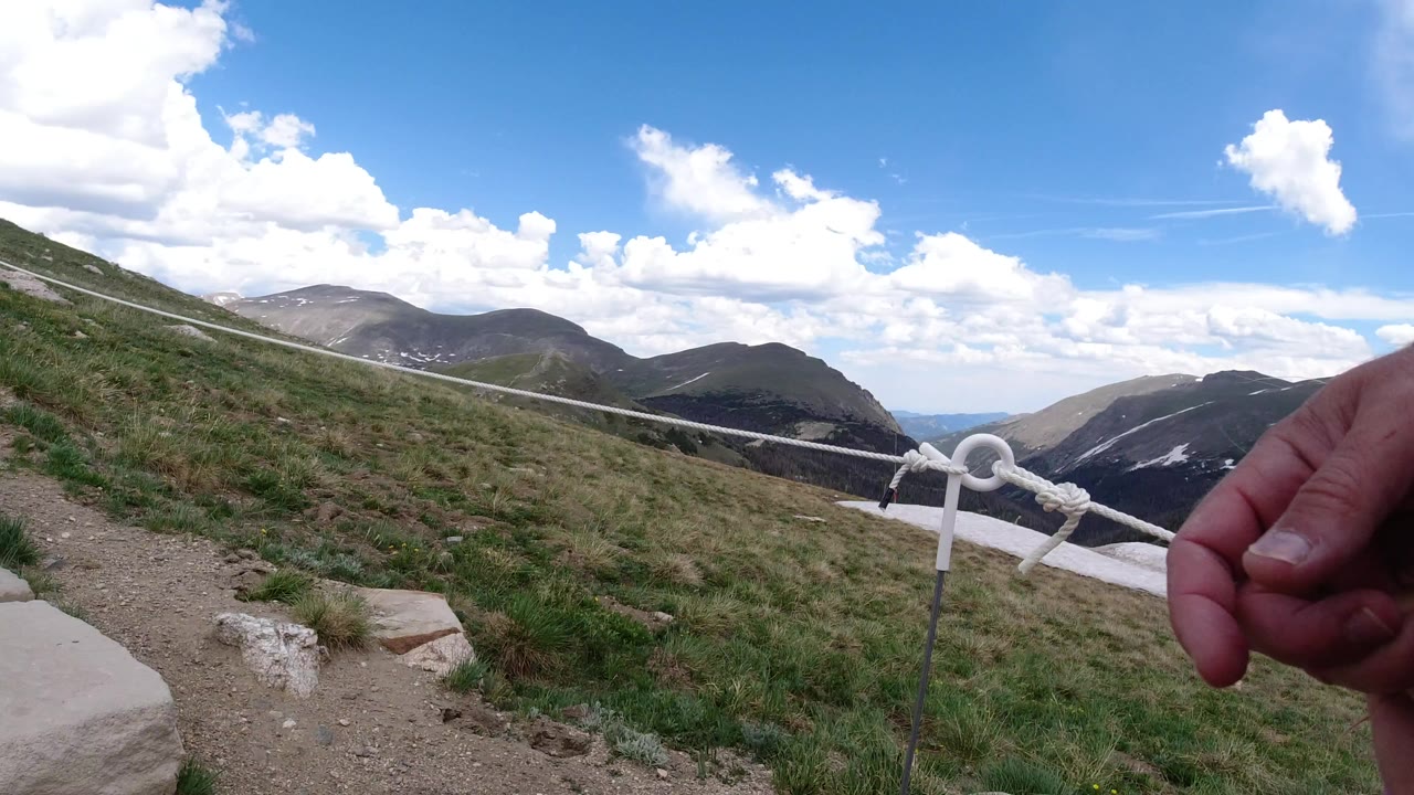 Mountain trail with rope handrail and an adult hand at the edge of frame.