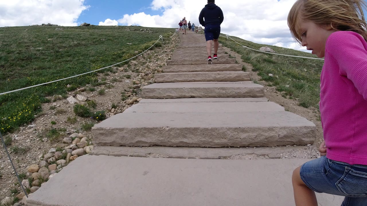 Child beside stone stairs as hikers climb a mountain path.