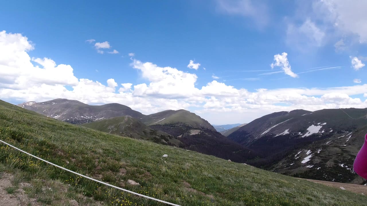 Wide view in Winter Park, Colorado of a grassy mountain slope, rope-lined trail, distant ridges with snow patches, and no visible people.