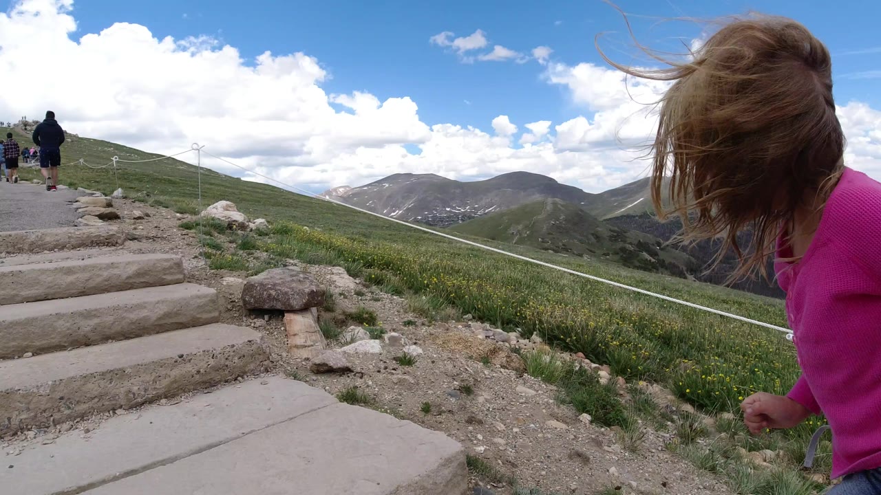 The child remains near the right edge of the frame while the path and steps lead uphill toward several people on a green mountainside in Winter Park, Colorado.
