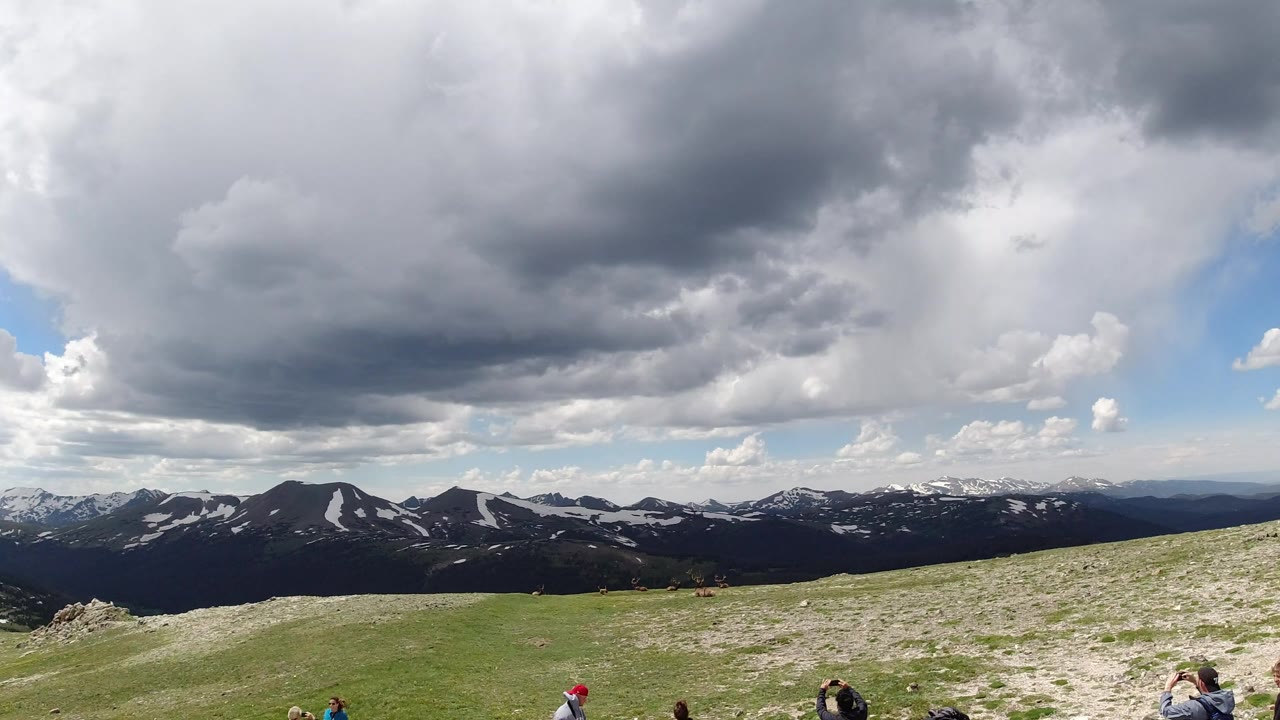 Wide mountain overlook with cloudy sky and people at the lower edge.