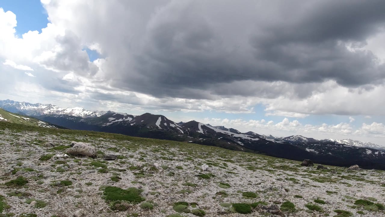 Tilted alpine landscape with dark cloud cover above snow-dotted mountains.