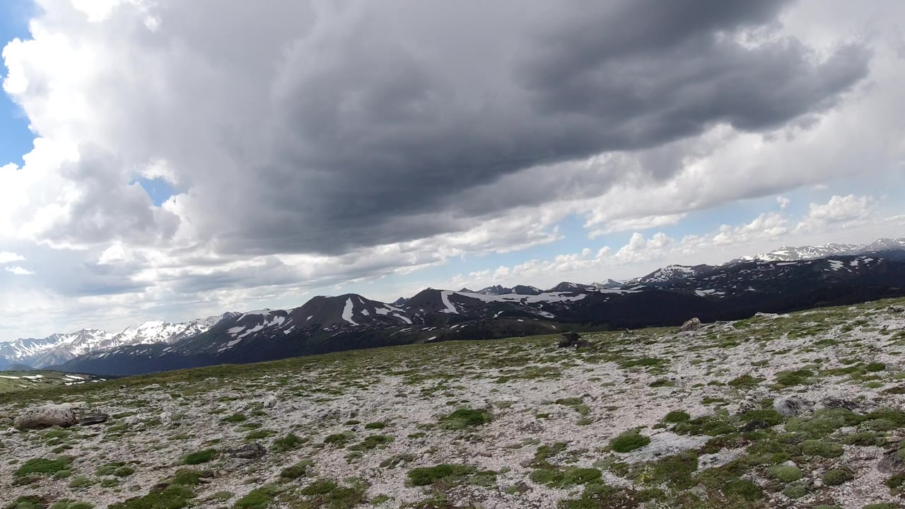 Winter Park, Colorado landscape with pale rocks and low green vegetation in the foreground, dark mountain ridges across the horizon, bright side sky, and no visible people.