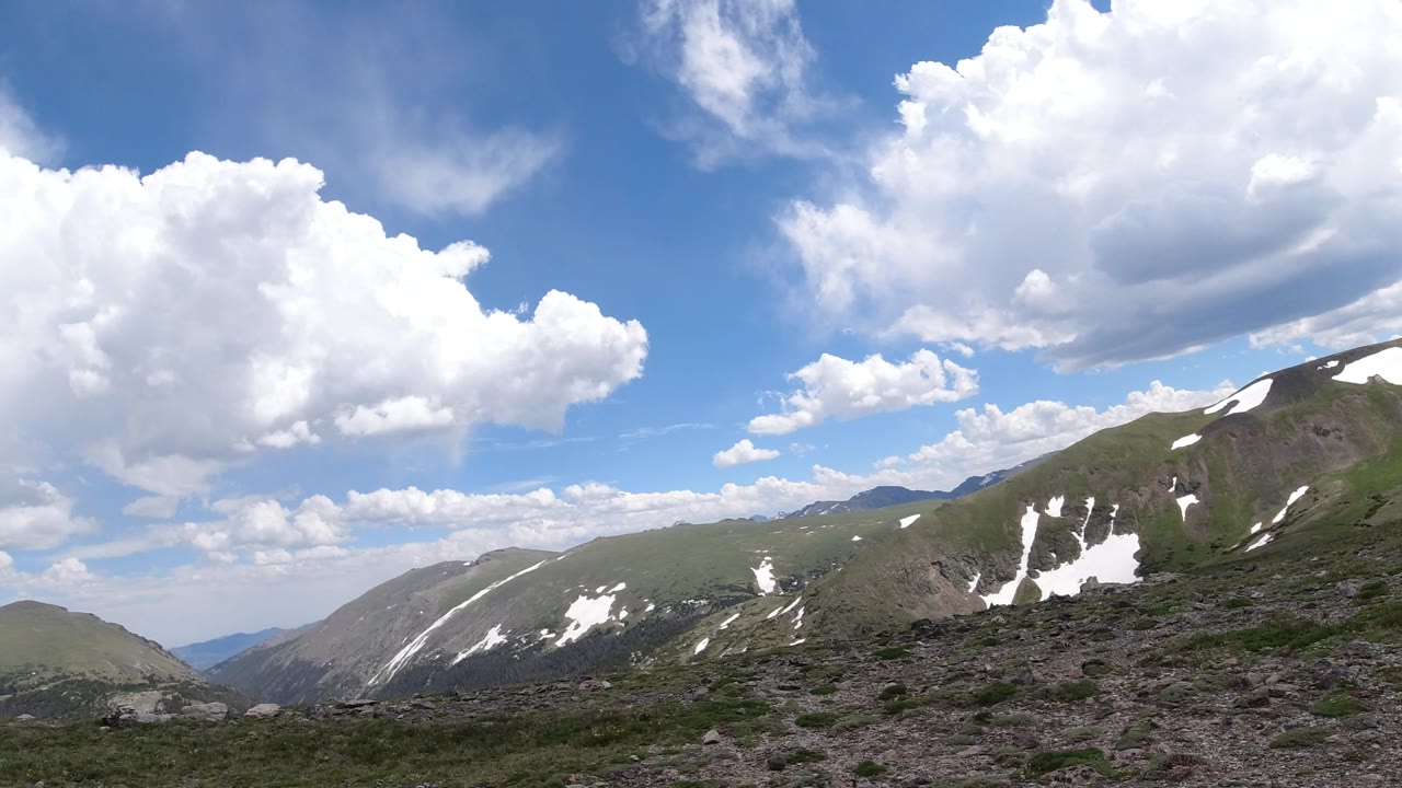 Wide Winter Park, Colorado landscape with a snow-marked ridge crossing the center, rocky tundra below, puffy clouds above, and no visible people.