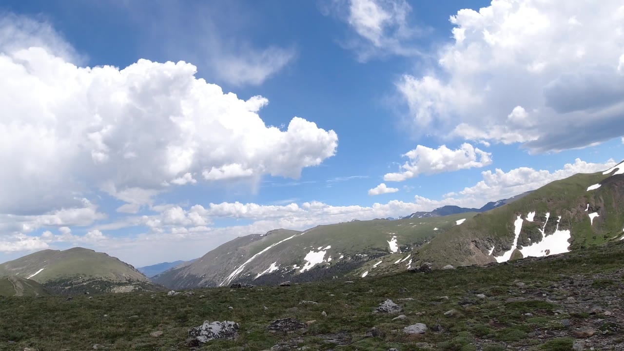 Rolling mountain ridges with white snow streaks and cloud cover.