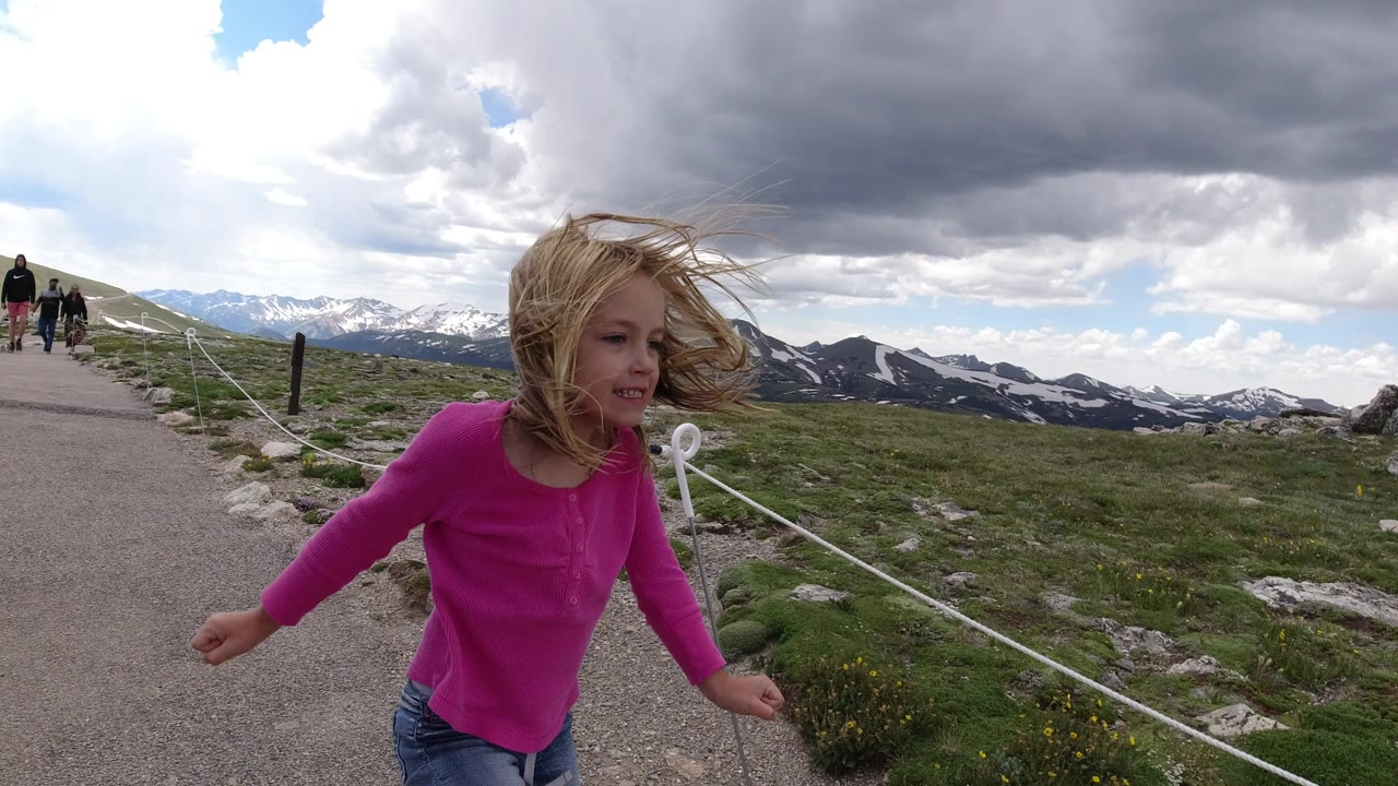 Blonde child in a pink shirt walking beside a mountain path.