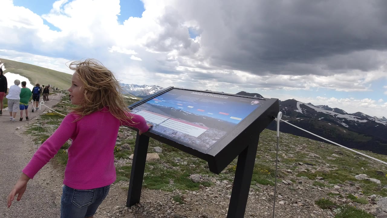 Young girl beside a mountain trail sign with tourists ahead.