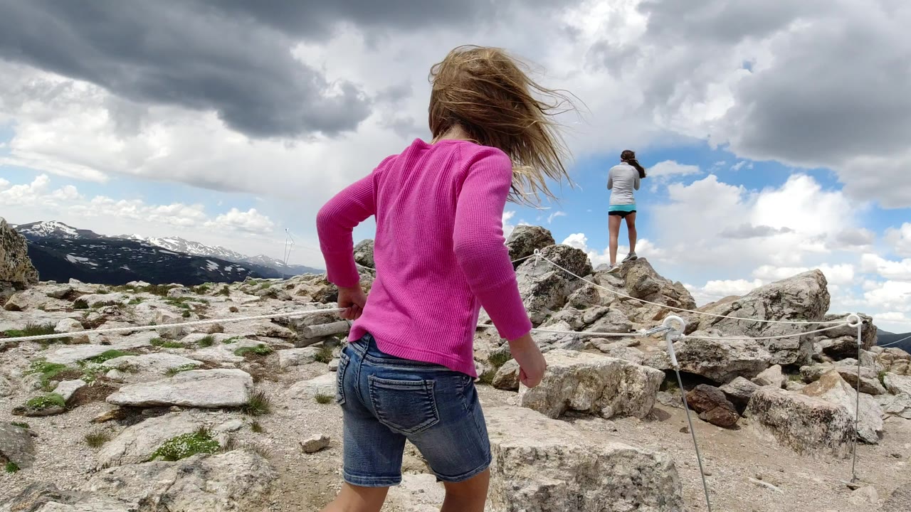 Child in a pink top walking across rocks toward an adult on a rocky overlook.