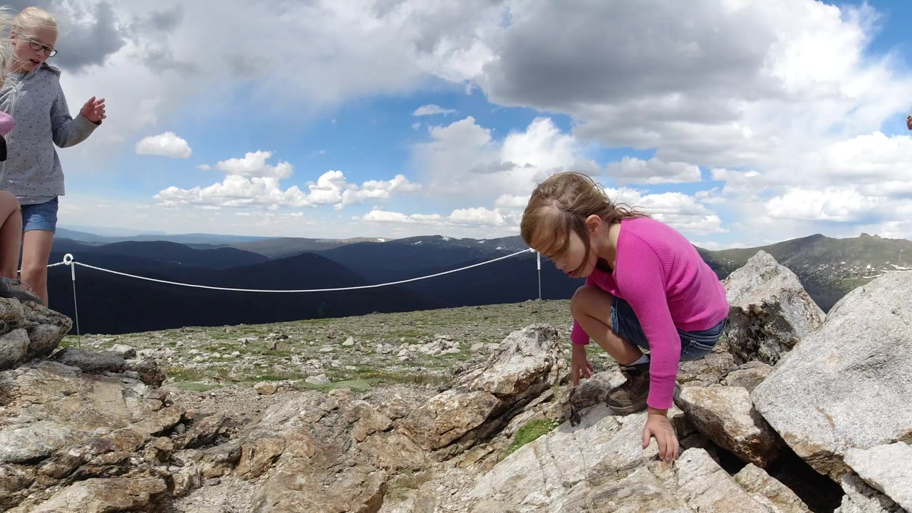 Child in a pink top climbs over pale rocks with mountains behind.