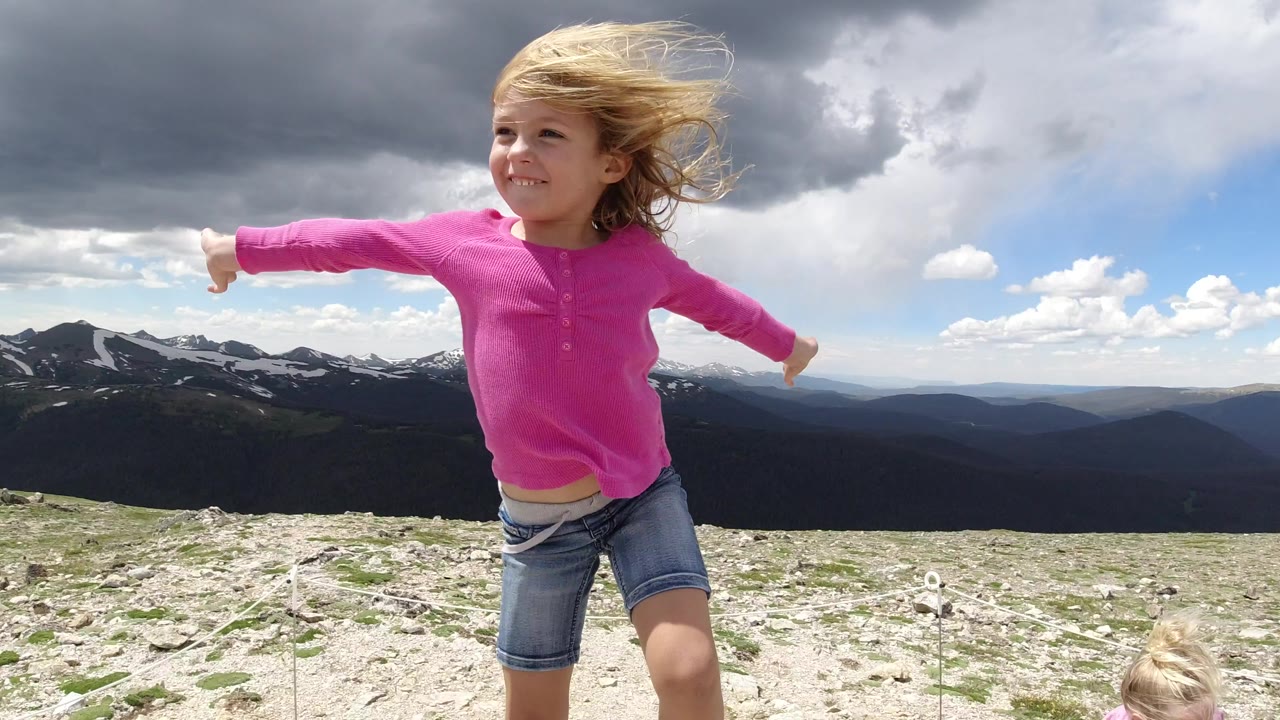 Young girl in pink standing on a windy mountain hilltop.