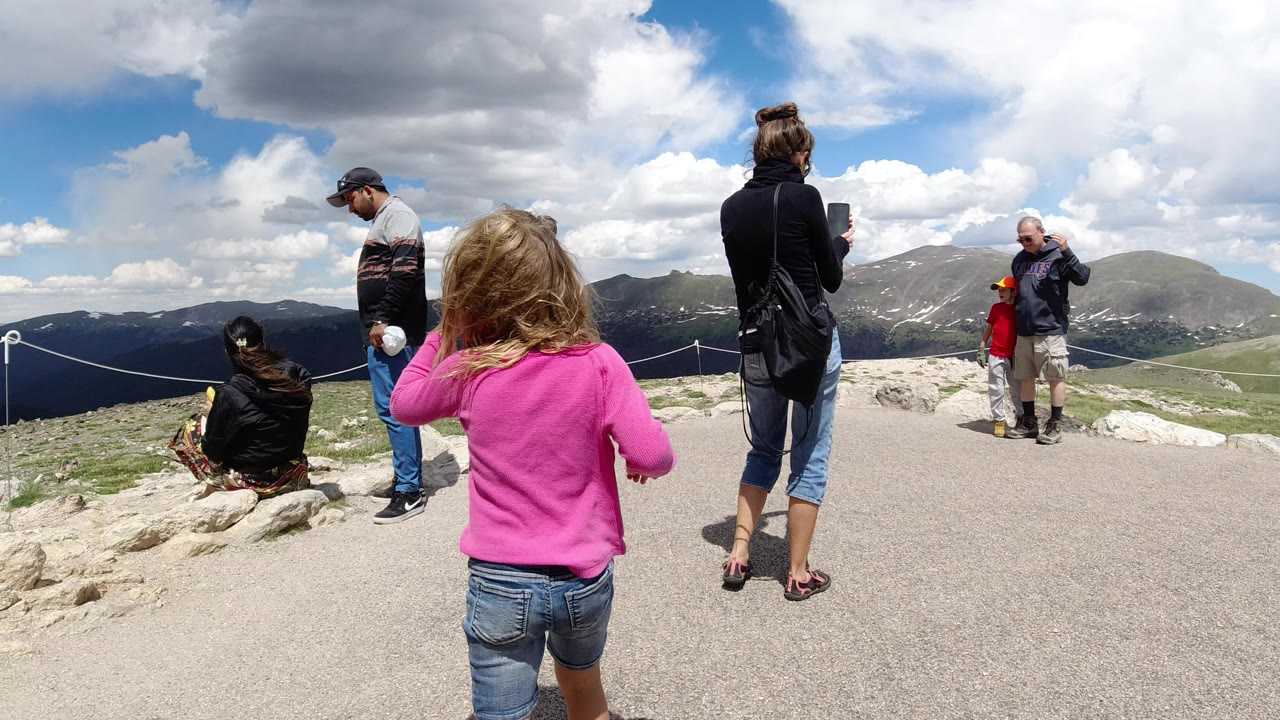 Girl in pink top walking toward family at a mountain overlook.