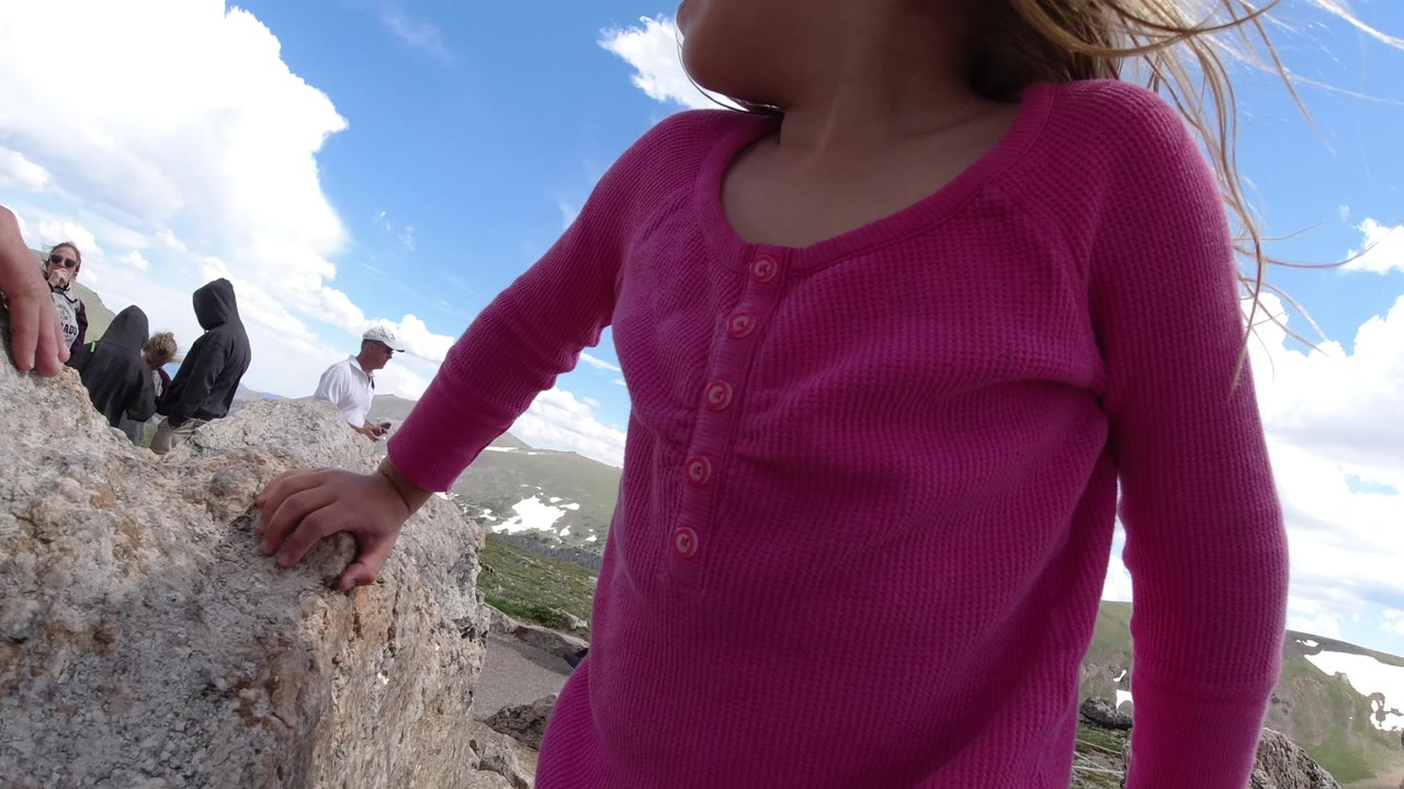 Close view of a child in a pink shirt climbing on rocks under a blue sky.