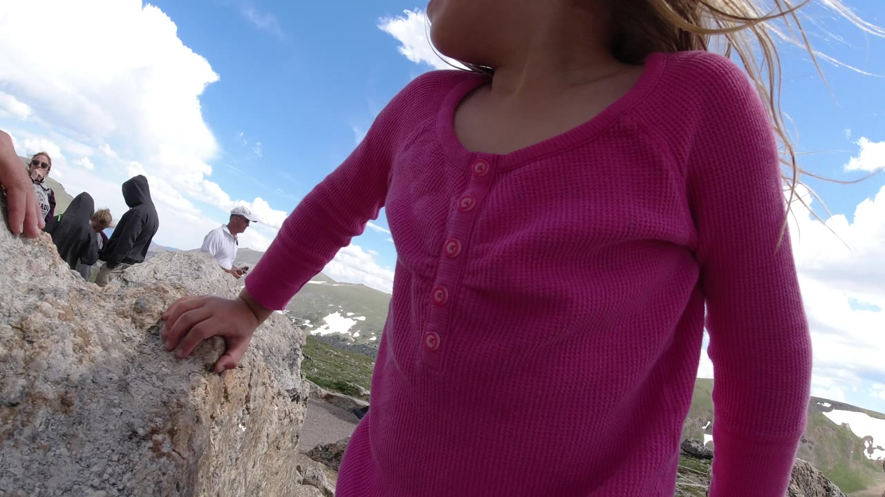 A second close frame in Winter Park, Colorado, keeps the child in pink at the rocky foreground while seated visitors and distant mountain slopes remain visible behind her.