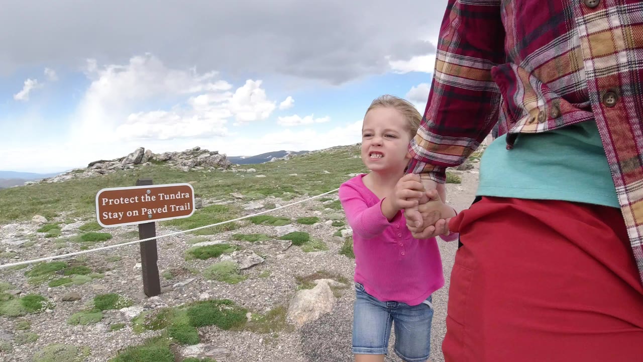 Young girl holding an adult woman's hand beside a roped rocky trail and tundra sign.