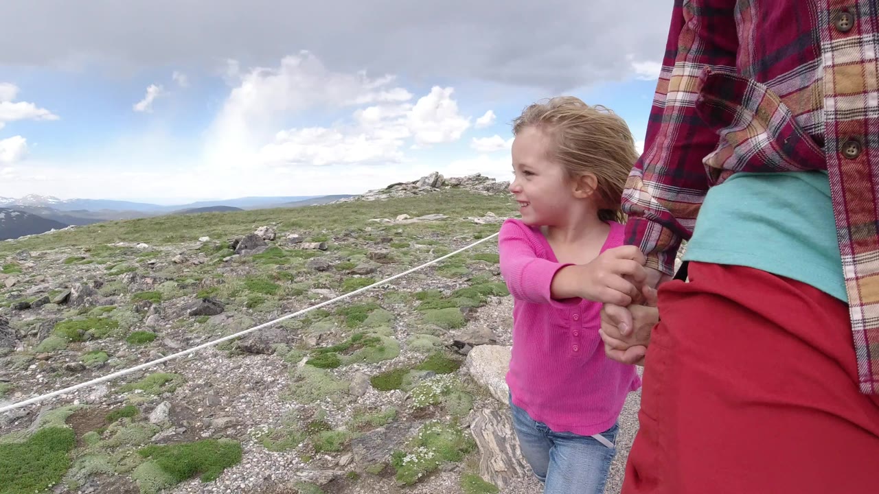 One second in, the girl looks toward the adult while holding her hand, with a white rope line crossing the rocky Winter Park mountain landscape behind them.